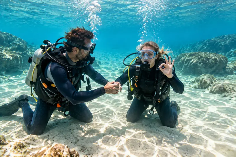 Instructor de buceo acompañando a una principiante en agua poco profunda sobre fondo de arena